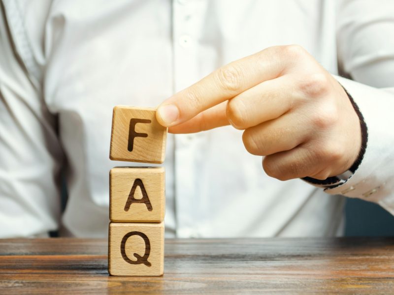 Businessman puts wooden blocks with the word FAQ (frequently asked questions)